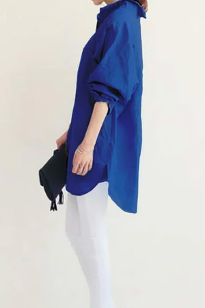 Woman wearing oversized blue linen shirt with rolled sleeves and white pants against plain background