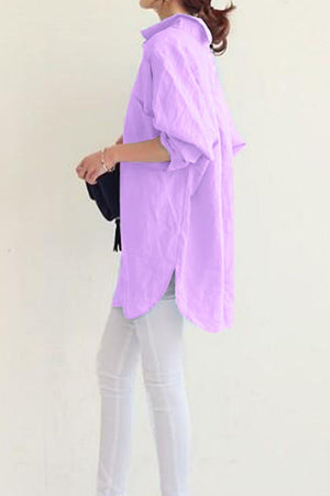Woman wearing a light purple oversized linen shirt with rolled-up sleeves and white pants, side view