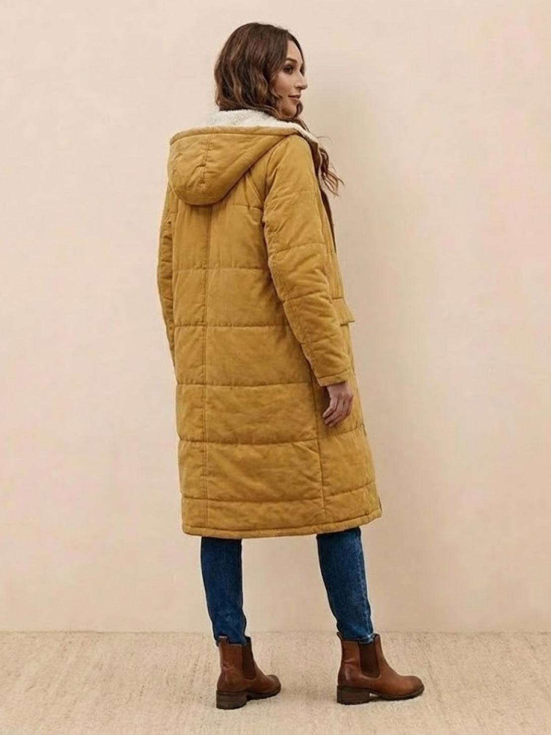 Woman wearing mustard Sherpa-lined hooded teddy coat with blue jeans and brown boots, back view