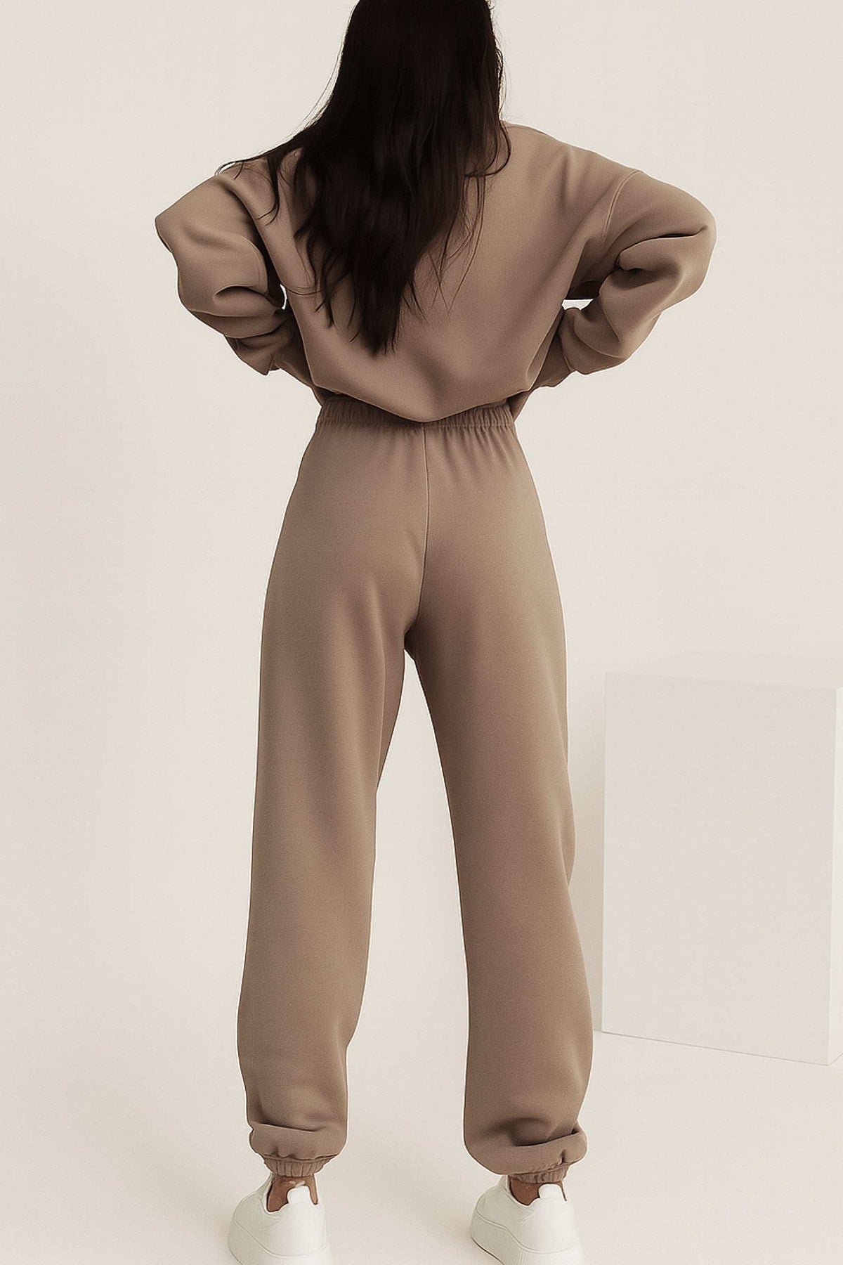 Back view of a woman wearing a neutral-toned cotton blend tracksuit with stretch waistband and cuffs, showcasing a relaxed yet tailored fit.