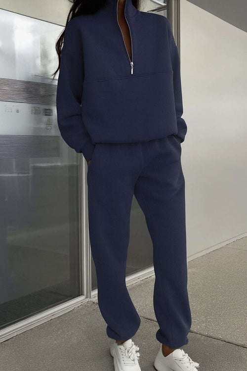 Woman wearing navy cotton blend tracksuit with zip neckline and relaxed fit pants.
