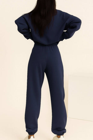 Woman wearing navy blue cotton blend tracksuit with long sleeves and elastic waist and cuffs, viewed from back.