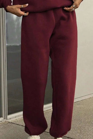Close-up of burgundy cotton blend tracksuit pants with hands in pockets on a sidewalk