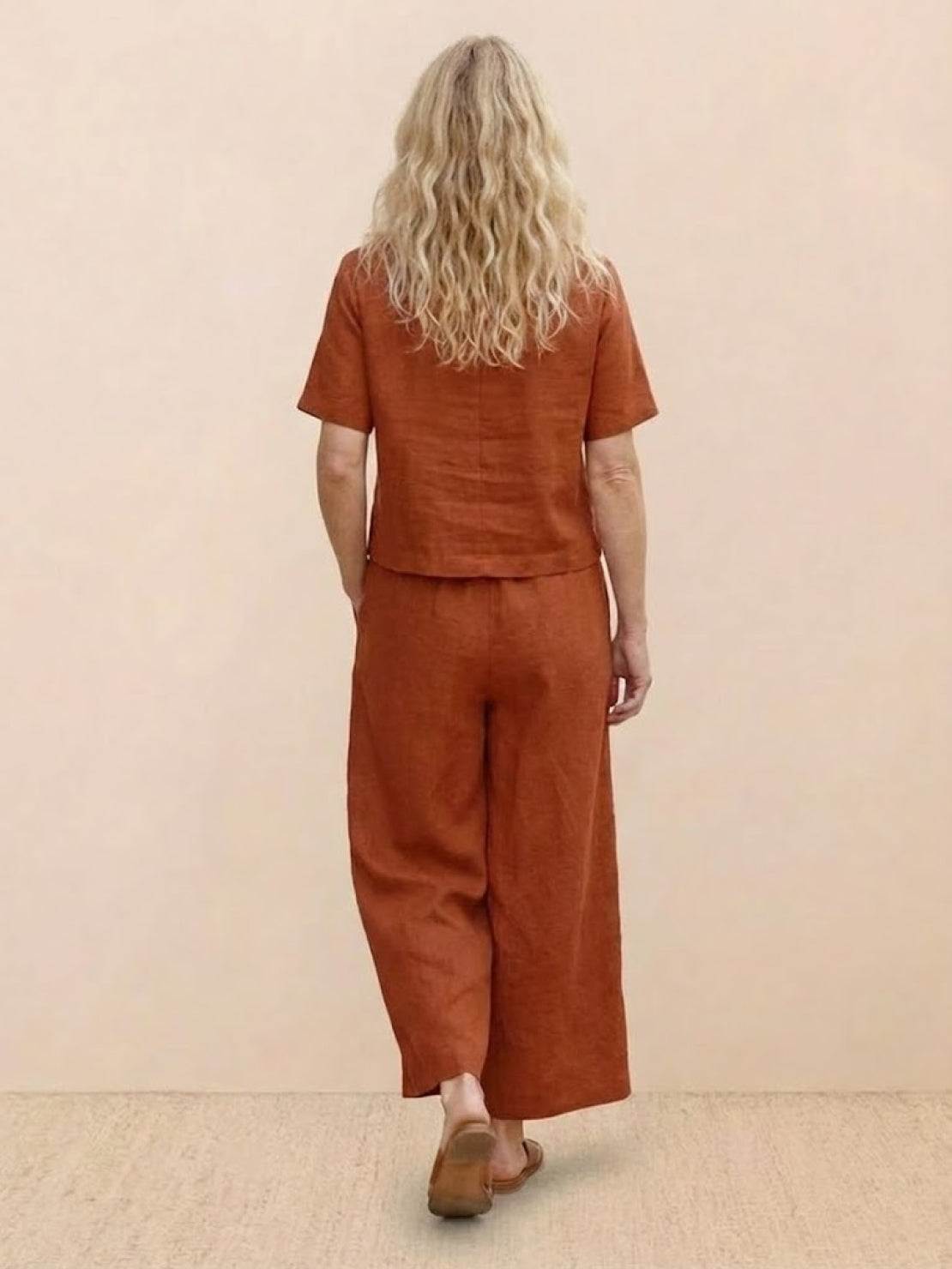 Woman wearing rust brown loose fit co-ord set with wide-leg pants and short-sleeve top, back view.