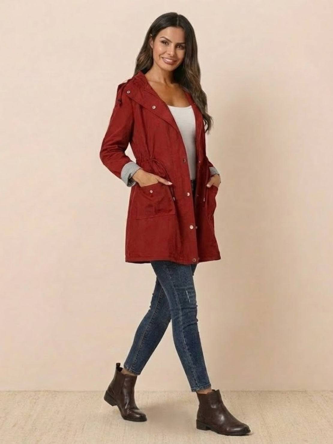 Woman wearing a red water resistant windbreaker jacket with hood and striped design, paired with jeans and brown boots