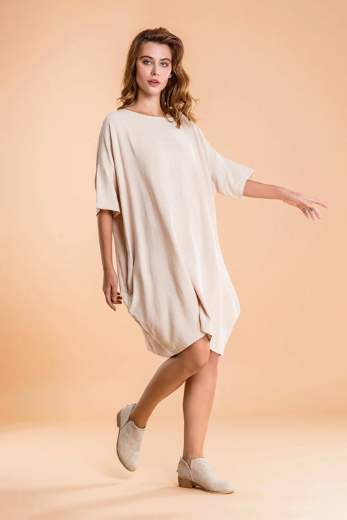 Woman wearing nude oversized premium linen ovoid dress with short sleeves and discreet pockets