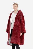 Woman wearing oversized ultra soft hooded blanket in deep red with front pockets and zipper closure