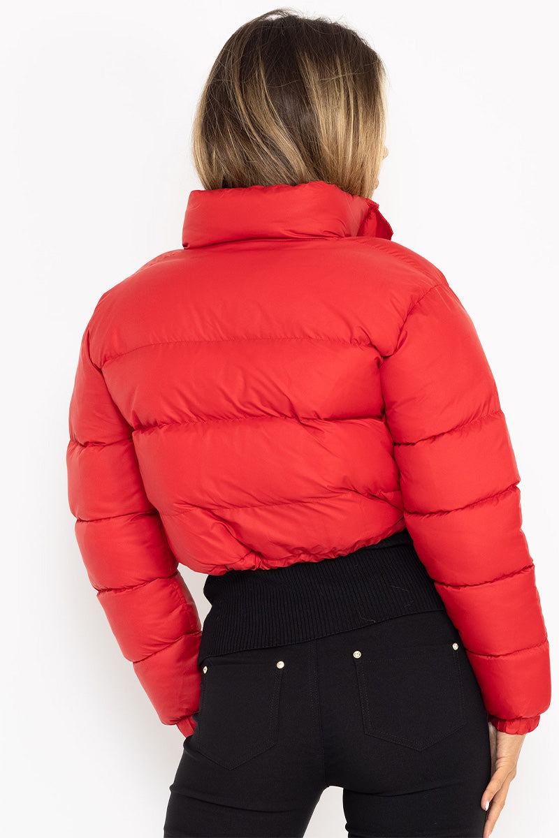 Woman wearing a red cropped puffer jacket with high collar and black pants, back view
