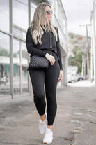 Woman wearing black Cozy Chic Two-Piece Sweatsuit set with long-sleeve top and fitted pants, white sneakers, and sunglasses walking outdoors