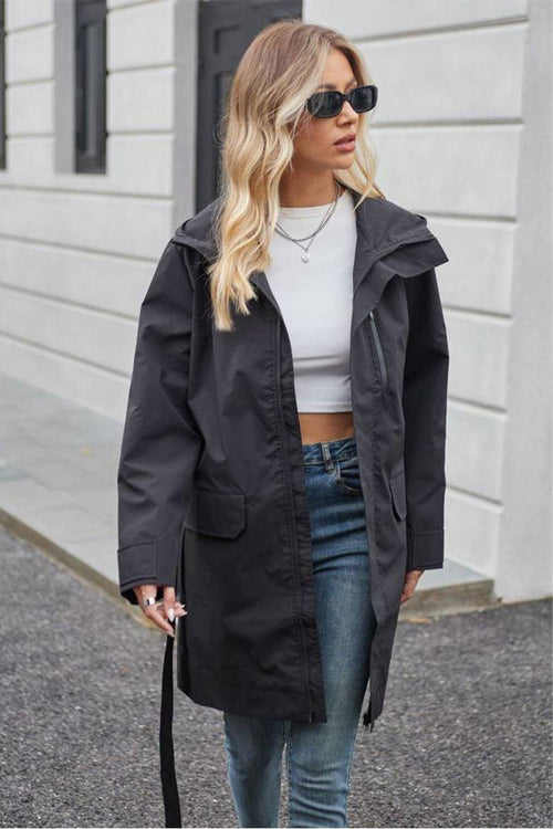 Woman wearing black water-resistant windbreaker trench jacket with belt and sunglasses outdoors