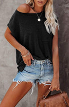 Woman wearing a black Easy Breezy Tunic Shirt with cap sleeves and front pocket paired with denim shorts and holding a brown handbag