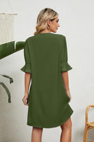 Back view of woman wearing olive green Dainty Charm Casual Ruffle Dress with ruffle sleeves in a minimal indoor setting
