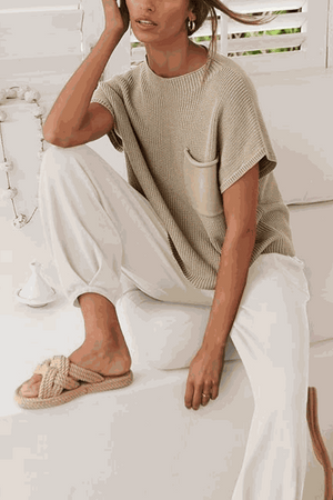 Woman wearing Comfy Couture Knit Sweater two-piece set with knit pullover and white pants sitting on couch