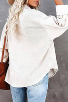 Woman wearing a beige sleek suede oversized button-down shirt with light blue jeans seen from the back