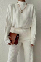 Timeless Striped Two-Piece knitwear set in soft white ribbed polyester with long sleeves and matching pants, styled with a brown handbag and gold necklace.