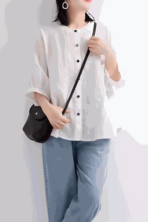 Woman wearing relaxed loose breathable linen blouse in white with rolled sleeves and black buttons paired with light blue jeans and black crossbody bag