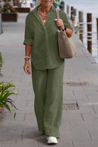 Woman wearing olive green relaxed shirt and trousers two-piece set walking outdoors with a beige crochet handbag.