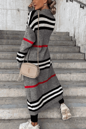 Cozy striped long knitted cardigan with oversized fit and red, black, and white stripes worn by woman on stairs