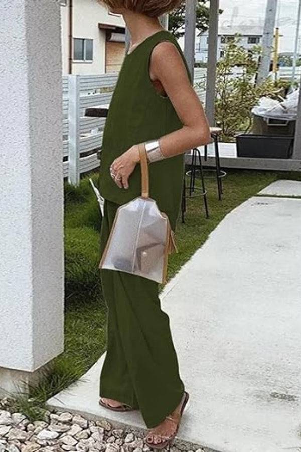Woman wearing loose solid color sleeveless two-piece set in olive green outdoors with transparent handbag and sandals