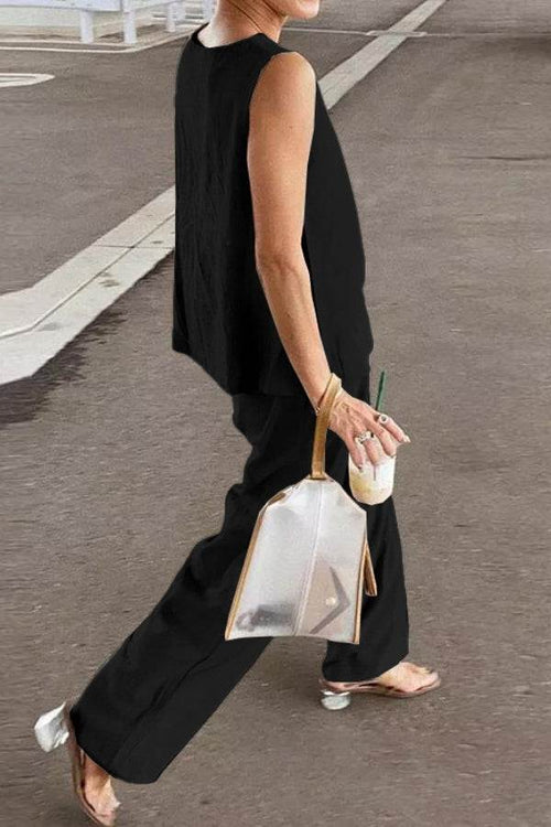 Woman wearing loose solid color black sleeveless two-piece set walking outdoors with transparent handbag and drink.