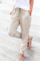 Woman wearing beige relaxed chic elastic ankles pants with drawstring waist and tapered elastic cuffs, paired with white top and sandals on outdoor steps