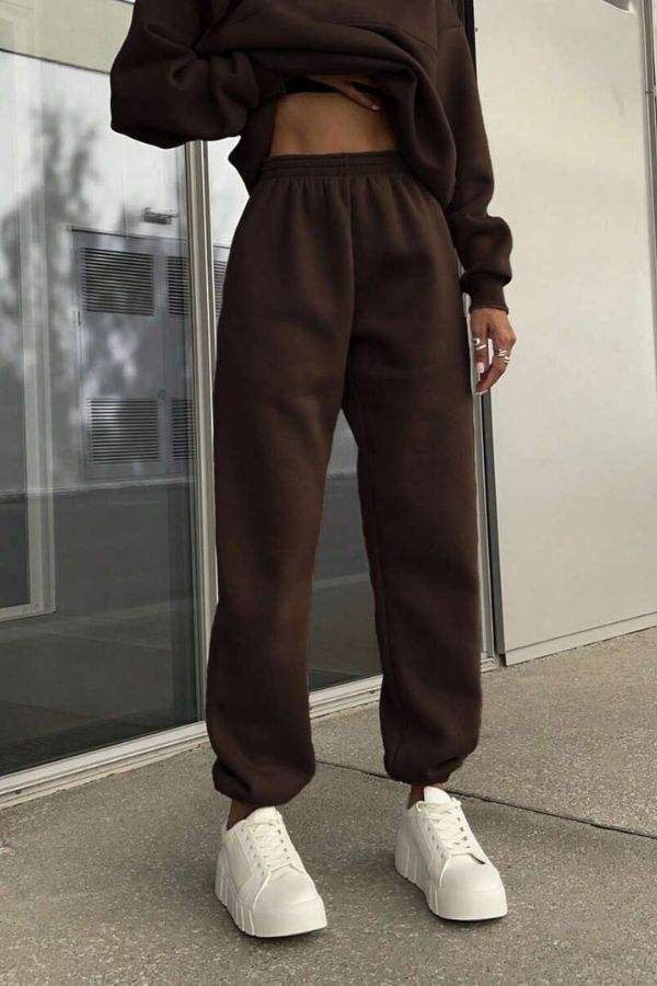 Woman wearing brown cotton-blended two-piece tracksuit pants with white sneakers outdoors.