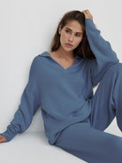 woman wearing blue plush and preppy two-piece lounge set seated against white wall