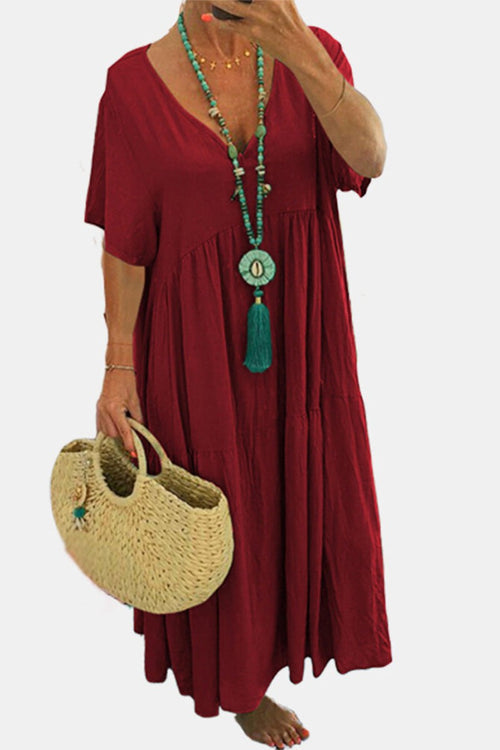 Woman wearing red V-neck two-tiered maxi swing dress holding straw handbag and turquoise necklace