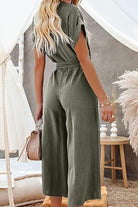 Back view of woman wearing olive green V-neck lace-up jumpsuit with tie belt and wide legs