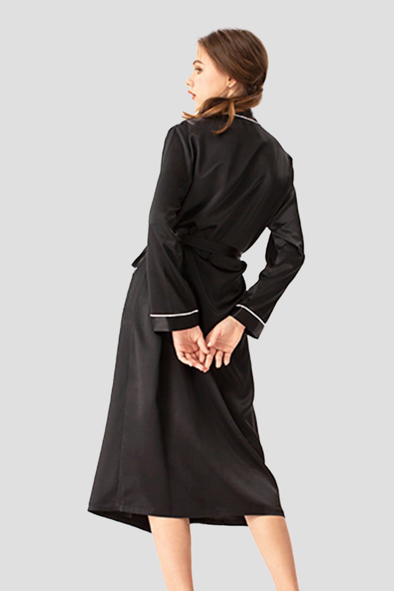 Woman wearing a black 100% mulberry silk belted classy nightgown with long sleeves and white trim on cuffs, viewed from the back.