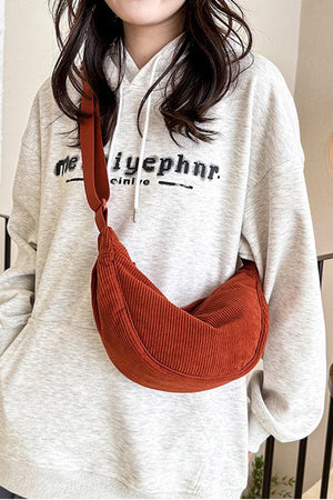 Rust-colored corduroy shoulder bag with adjustable strap worn crossbody with casual hoodie.