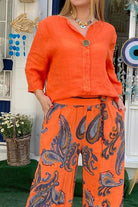 Woman wearing vibrant orange long sleeve top and paisley patterned pants from Vibrant Fusion Two-Piece Set