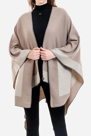 One size elegant knitted poncho in two-tone beige and taupe colors with flowing silhouette worn over black outfit