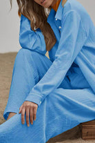 Woman wearing light blue linen blend two-piece set with long-sleeve top and wide-leg pants sitting outdoors