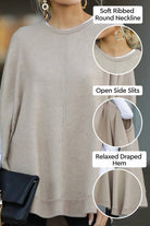 Elegant poncho pullover in light beige with soft ribbed round neckline, open side slits, and relaxed draped hem, styled with gold hoop earrings and black clutch bag.
