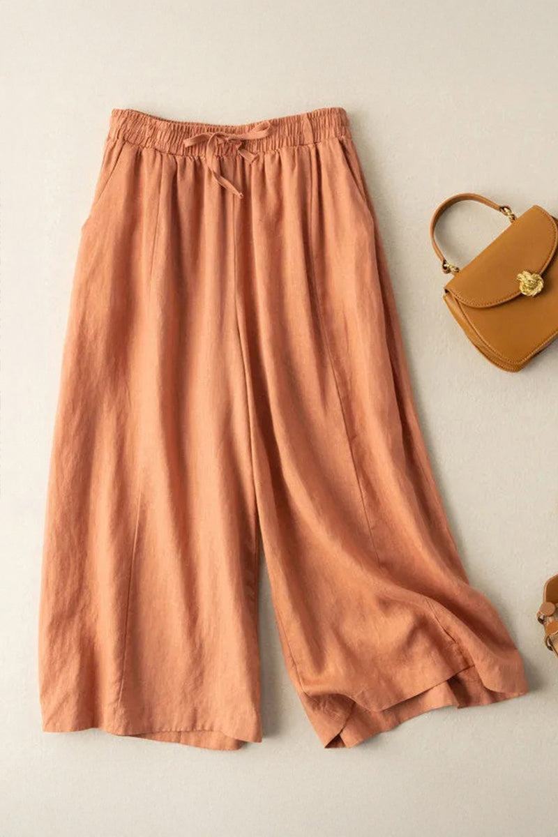 Cotton Linen Tuscany wide-leg linen blend trousers in warm terracotta color with elastic waistband and drawstring detail next to a tan handbag on beige background