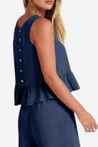 Woman wearing navy linen-like feel sleeveless top and pants set with buttoned back and peplum hem detail