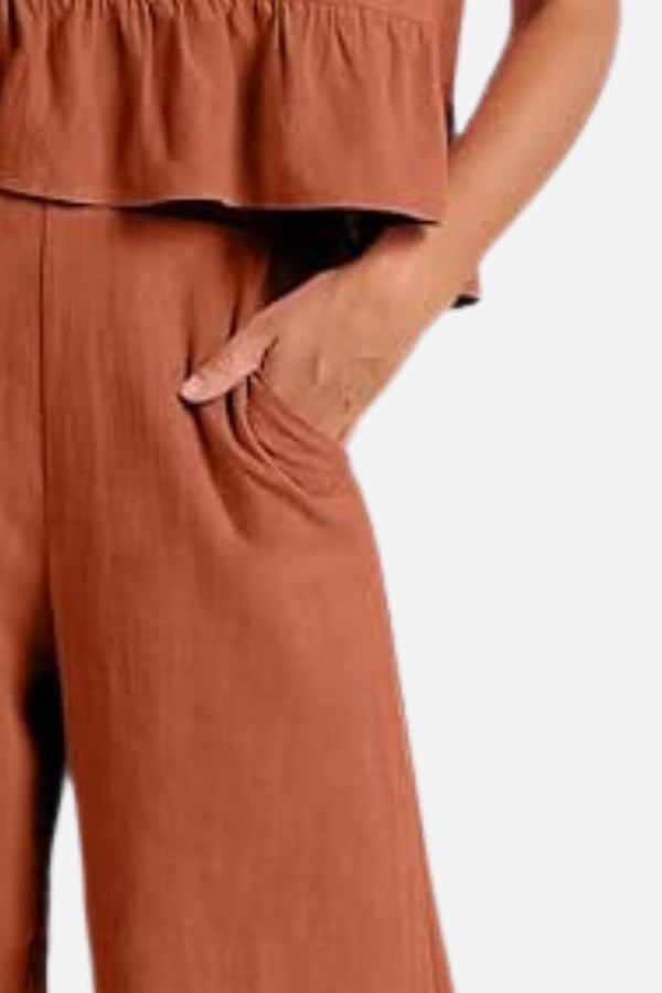 Close-up of rust-colored lightweight linen-like feel set pants with hand in pocket