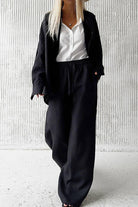 Woman wearing 100 Cotton Wanderlust black two-piece cotton set with white blouse against textured wall background