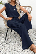 Woman wearing elegant navy blue two-piece set with lace sleeve details sitting on a wicker chair outdoors