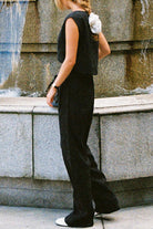 Woman wearing black cotton-linen blend two-piece outfit with wide-leg pants and sleeveless cropped top standing by water fountain