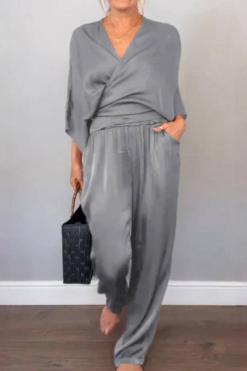 Woman wearing soft grey Satin Wrap Lounge two-piece set with V-neck top and relaxed pants, holding black handbag.