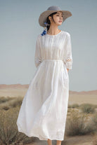 Woman wearing a white 100% linen coastal shift dress with long sleeves and hat in a natural outdoor setting