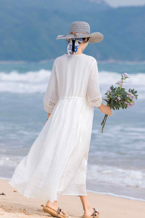 woman wearing 100% linen coastal shift dress walking on beach with hat and flowers