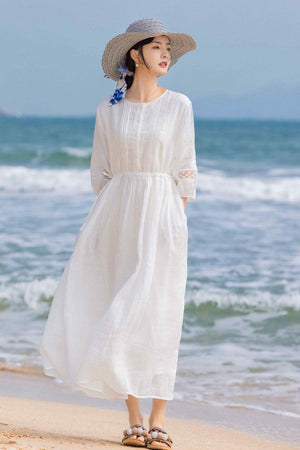 woman in white 100% linen coastal shift dress on beach with straw hat and sandals