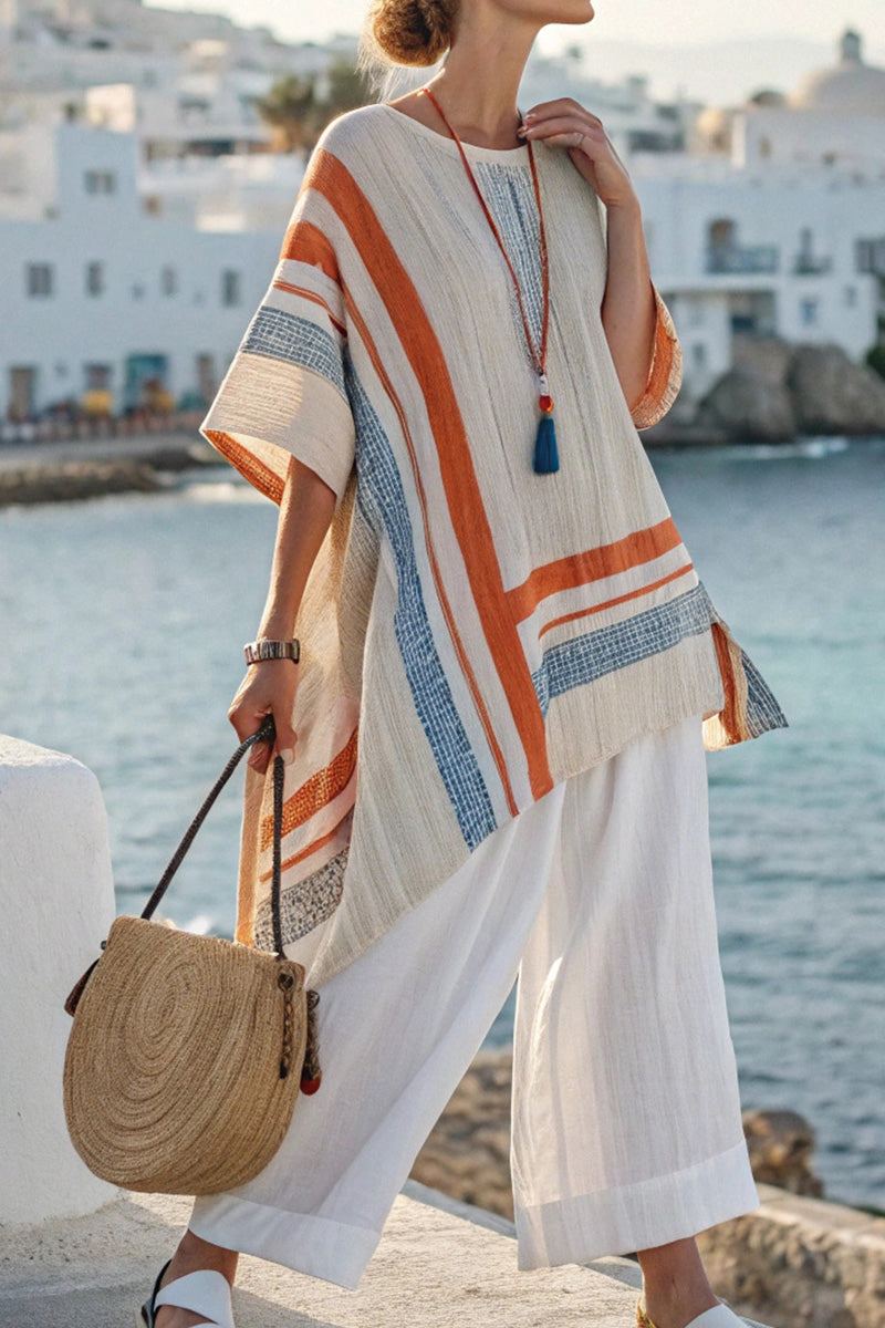 Woman wearing Coastal Comfort Linen two-piece set with a loose, colorful striped top and white wide-leg pants by the seaside with a round woven bag.