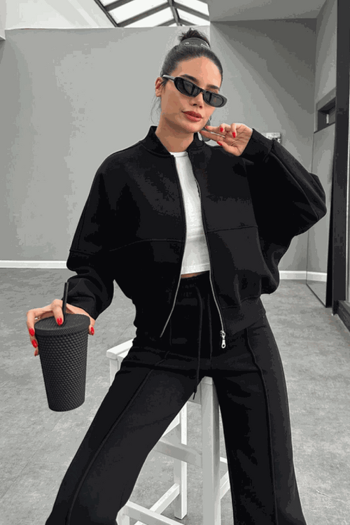 Woman wearing The Voyager Zip Set black zip-front sweatshirt and wide-leg joggers holding a drink cup, styled for travel and casual wear