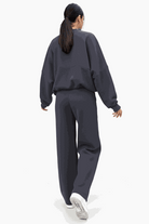 Woman wearing The Voyager Zip Set in dark charcoal, featuring a relaxed zip-front sweatshirt and wide-leg joggers with pockets, styled for comfort and travel.