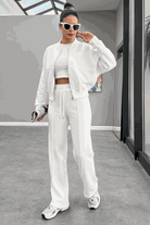 Woman wearing The Voyager Zip Set white zip-front sweatshirt and wide-leg joggers with sneakers in a modern indoor setting