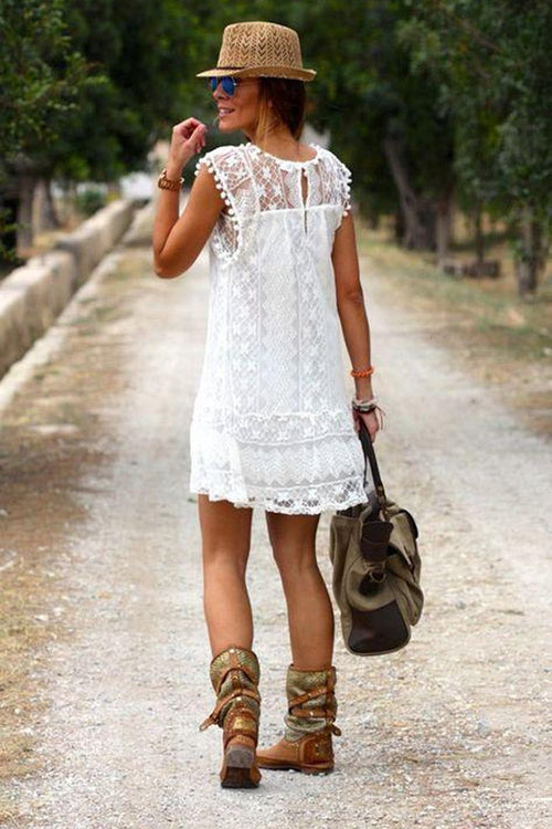 Woman wearing white pom pom lace mini dress with sleeveless design and carrying a bag on a path outdoors